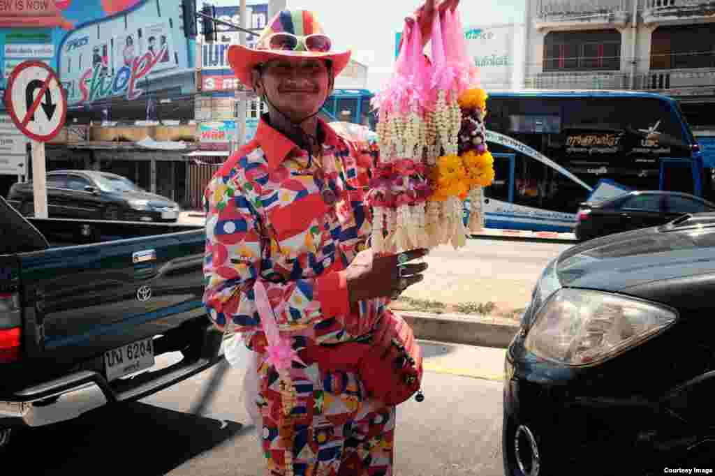 A man dressed in a colorful suit sporting the flags of ASEAN countries sells flower garlands at a set of traffic lights in Pranburi, Prachuap Khiri Khan province in Thailand, July 11, 2015. (Photo taken by Matthew Richards/Thailand)