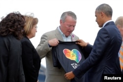 President Barack Obama, right, receives a T-shirt from Orlando Mayor Buddy Dyer, center, as he arrives in Orlando to meet with families of victims of the Pulse nightclub shooting, in Florida, June 16, 2016.