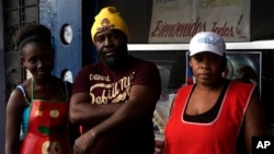 Haitian immigrant Wilthene Pierre is pictured with two of his cooks Emily, left, and Violette Novembre, in front of the Kriskapab Baborijinal Haitian restaurant in Tijuana, Mexico, Nov. 22, 2018. The cafe serves dishes of coconut rice, mashed plantains and goat stew.