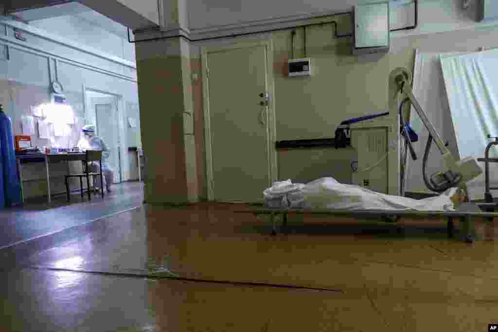 A medic wearing a special suit to protect against coronavirus fills documents as a body of a COVID-19 victim lies on a stretcher at an ICU of a hospital in Volgograd, Russia, Nov. 21, 2021.