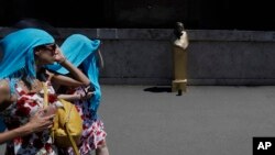 Tourists wear a scarf over their head to protect themselves from the sun as they walk past a street performer impersonating an Egyptian sphinx, in Rome, Thursday, June 27, 2019. 