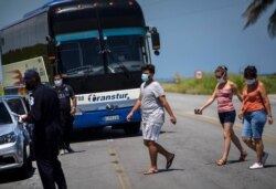 Residentes con máscaras caminan hacia la policía que tomará la temperatura corporal en un puesto de control donde antes de ingresar a la provincia de La Habana, Cuba, el lunes 10 de agosto de 2020