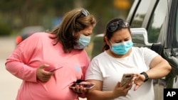 FILE -- Women wear masks as they check a mobile phone in Houston, Texas.