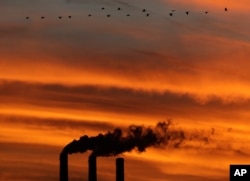 FILE - A flock of Geese fly past the smokestacks at the Jeffrey Energy Center coal power plant as the suns sets near Emmett, Kansas.