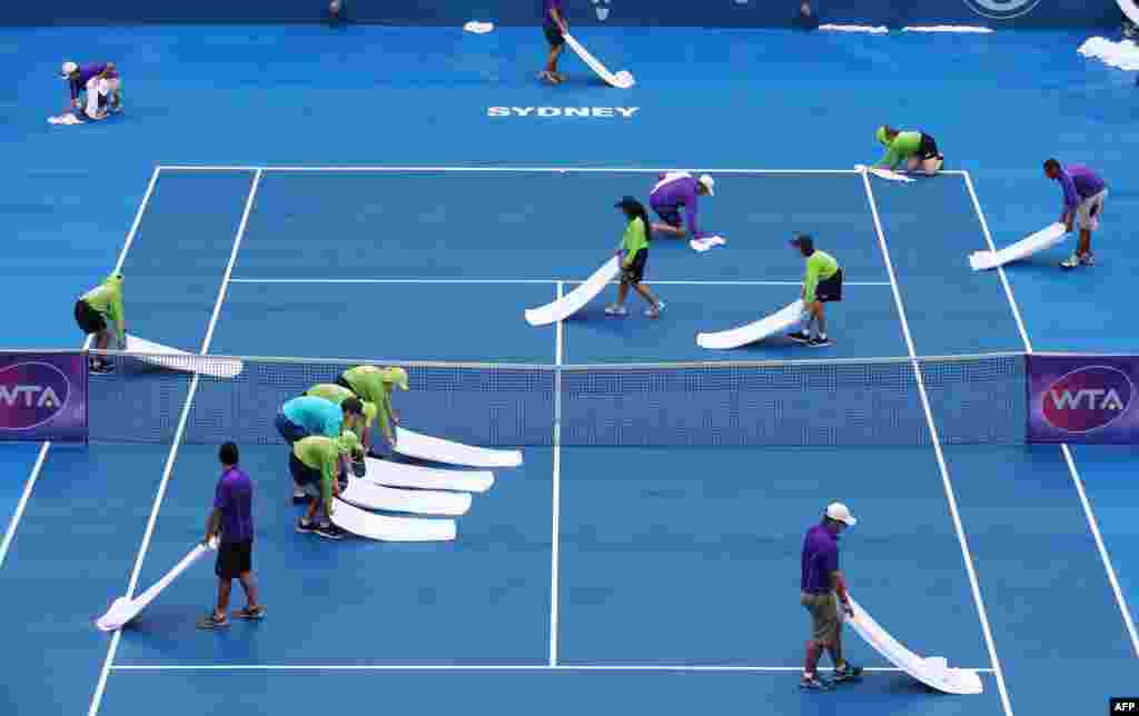 Nhân viên cố gắng lau khô sân quần vợt sau cơn mưa không ngớt vào ngày đầu của cuộc thi đấu giải quần vợt quốc tế ở Sydney, Australia.