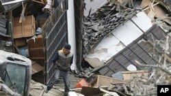 A man walks on the debris in Ishinomaki city, Miyagi prefecture after a powerful 7.1 aftershock rocked that area of Japan, April 8, 2011