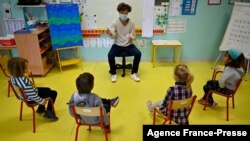 FILE - In this file photo taken on May 12, 2020, a teacher wearing a protective mask teaches children in her classroom at Champ l'Eveque public school in Bruz, western France. 