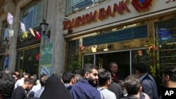 FILE - Iranians stand in front of a bank, hoping to buy U.S. dollars at the new official exchange rate announced by the government, in downtown Tehran, April 10, 2018.