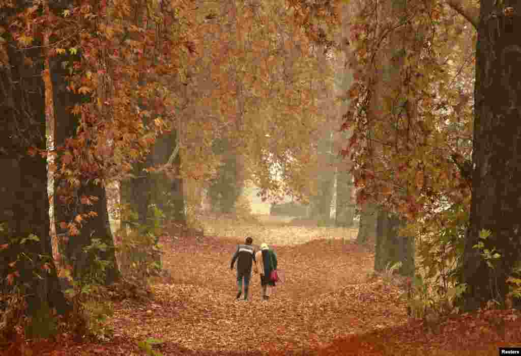 A couple walks on a path filled with fallen leaves of Chinar trees in a garden in Srinagar, India-controlled Kashmir.