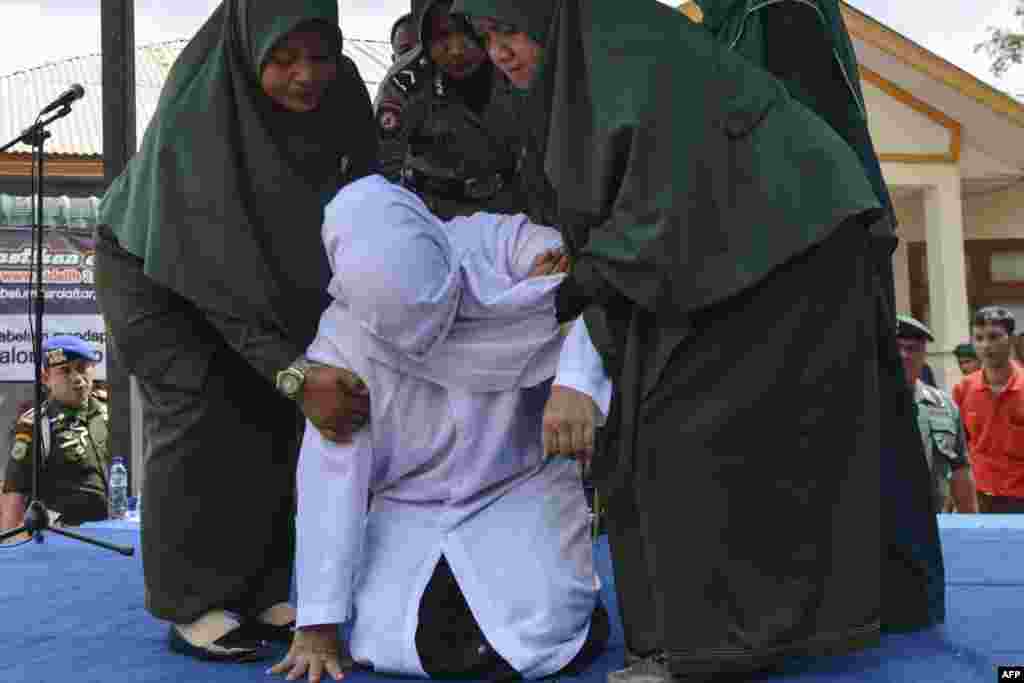 An 18-year-old Indonesian woman (C) is assisted by Sharia police after being caned in public in Banda Aceh as punishment for being caught cuddling with her boyfriend.