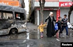 FILE - A woman with children walks by a vehicle that was damaged during the clashes between security forces and Kurdish militants, in Baglar district, which is partially under curfew, in the Kurdish-dominated southeastern city of Diyarbakir, Turkey, March 15, 2016.