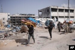 FILE —Palestinians carry their belongings after visiting their houses destroyed in the Israeli offensive on Khan Younis, Gaza Strip, March 6, 2024.