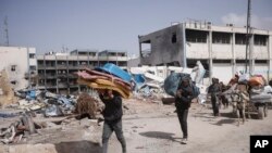 6일 가자지구 칸 유니스의 파괴된 건물들 앞에서 팔레스타인인들이 가재도구 등을 짊어지고 이동하고 있다.