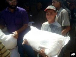 FILE - A boy holds a sack of food aid after aid agencies dropped via crane food across the Jordan-Syria border to community leaders charged with distributing equitably the supplies to the 64,000-person refugee camp called Ruqban.