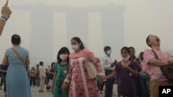 Tourists visit a sightseeing spot as the Marina Bay Sands Hotel in the background is shrouded with haze in Singapore, June 22, 2013. 