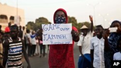 Un homme brandit une affiche avec inscription : "C’est fini pour Yahya Jammeh !" au milieu des manifestants en liesse à Serrekunda, Gambie, 19 janvier 2017.