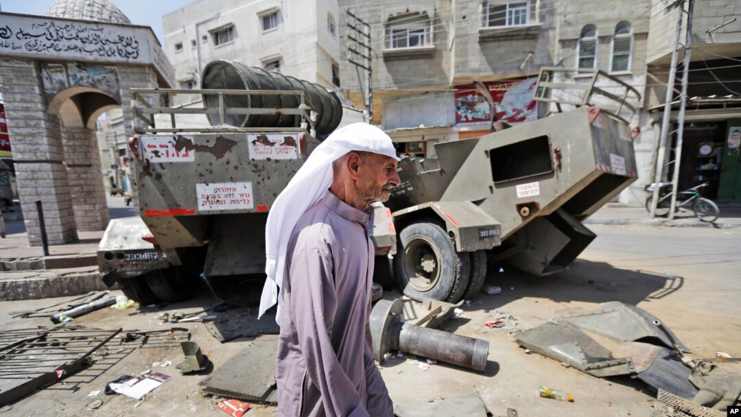 Seorang warga Palestina berjalan di dekat kendaraan militer Israel yang rusak di Khan Younis, Jalur Gaza Selatan (11/8). 