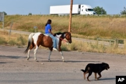 A girl rides a horse near a highway accompanied by a dog on the Crow Indian Reservation in Crow Agency, Mont. on Wednesday, Aug. 26, 2020. Youth suicide among the state’s 12 federally recognized tribes is more than five times the statewide rate for the same age group.