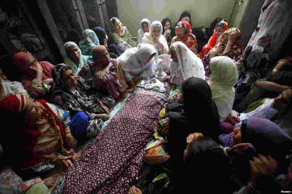 Relatives sit around the body of a boy who was killed in a Wednesday night bomb blast in Karachi August 7, 2013. 