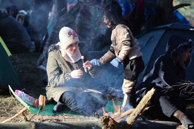 A woman and her child eat as they gather with other migrants from the Middle East and elsewhere at the Belarus-Poland border near Grodno, Belarus, Nov. 9, 2021.