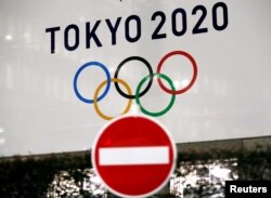FILE - A banner for the Tokyo 2020 Olympics is seen behind a traffic sign, following an outbreak of the coronavirus disease (COVID-19), in Tokyo, Japan, March 23, 2020.
