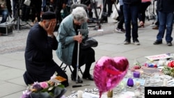 A Jewish woman named Renee Rachel Black and a Muslim man named Sadiq Patel react next to floral tributes in St Ann's Square in Manchester, May 24, 2017.