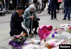 FILE - A Jewish woman named Renee Rachel Black and a Muslim man named Sadiq Patel react next to floral tributes in St Ann's Square in Manchester, May 24, 2017.