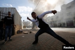 FILE - A Palestinian youth throws stones at Israeli troops following an anti-Israel demonstration in solidarity with al-Aqsa mosque in the West Bank city of Hebron, Nov. 14, 2014.