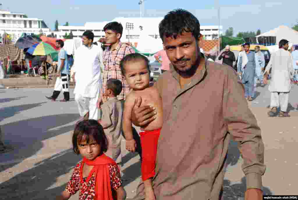 دھرنے میں شریک ایک شخص چھوٹی بچی اٹھائے ہوئے۔