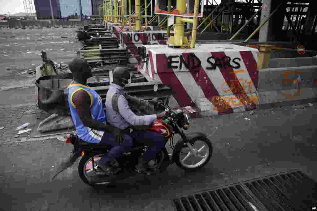 People drive past burnt toll gates with anti police slogans sprayed across, in Lagos Friday, Oct. 23, 2020. Resentment lingered with the smell of charred tires Friday as Nigeria&#39;s streets were relatively calm after days of protests over police abuses, whi