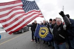 FILE - A General Motors employee holds an American flag as colleagues gather outside the plant, March 6, 2019, in Lordstown, Ohio. The plant was idled.