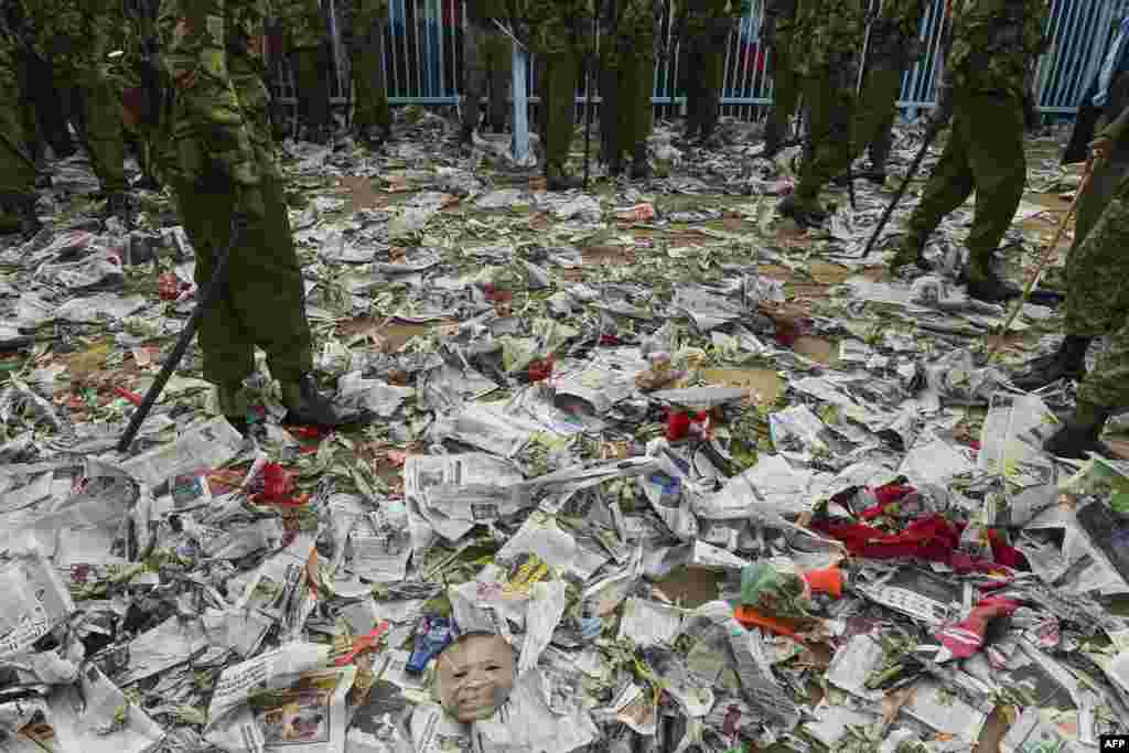 Policemen walk through scattered newspapers and a mask of Kenya's new president (Bottom L) following a stampede outside Kasarani stadium in Nairobi, after supporters of President Uhuru Kenyatta tried to get into the venue to attend his inauguration ceremony.