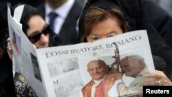 FILE - A woman reads a copy of the Vatican newspaper L'Osservatore Romano as she waits for the canonization ceremony in St Peter's Square at the Vatican, Apr. 27, 2014.