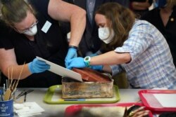 FILE - Kate Ridgeway and Sue Donovan, conservators with the Virginia Department of Historic Resources, remove one of three books found in a time capsule recovered from Confederate General Robert E. Lee's monument in Richmond, Virginia, Dec. 22, 2021.