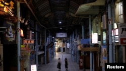 FILE - Passersby wearing protective face masks, amid the COVID-19 pandemic, walk at a shopping arcade in the prefectural capital Naha, on the southern island of Okinawa, Okinawa prefecture, Japan, Oct. 24, 2021.