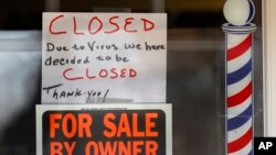 Obavještenje u berbernici u Mičigenu da je zatvorena zbog virusa, iznad znaka na kojem piše da vlasnik prodaje objekat (Foto: AP/Paul Sancya) 