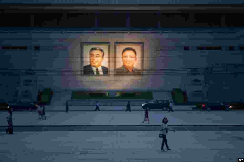 북한 평양의 김일성 광장에서&nbsp;시민들이​ 김일성 부자의 사진 앞으로 걸어가고 있다.