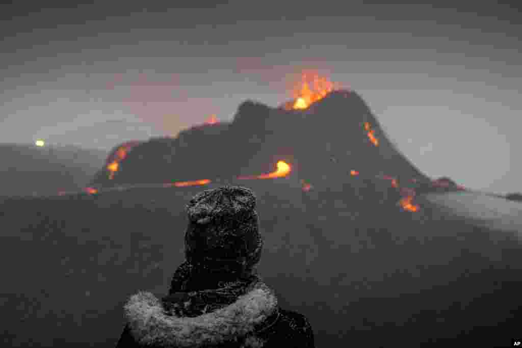 A person watches as lava flows from an eruption of a volcano on the Reykjanes Peninsula in southwestern Iceland, March 24, 2021.