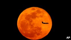 A plane descending into Newark Liberty International Airport crosses over the full moon rising seen from Eagle Rock Reservation, Wednesday, March 23, 2016, in West Orange, N.J. 