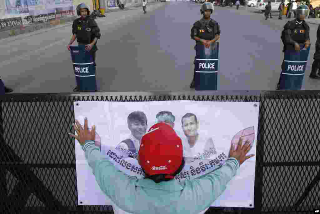 A supporter places a poster calling for the release of the imprisoned activists in front of riot police officers standing guard at a congested street near Phnom Penh Municipality Court, in Phnom Penh, Cambodia, May 30, 2014.