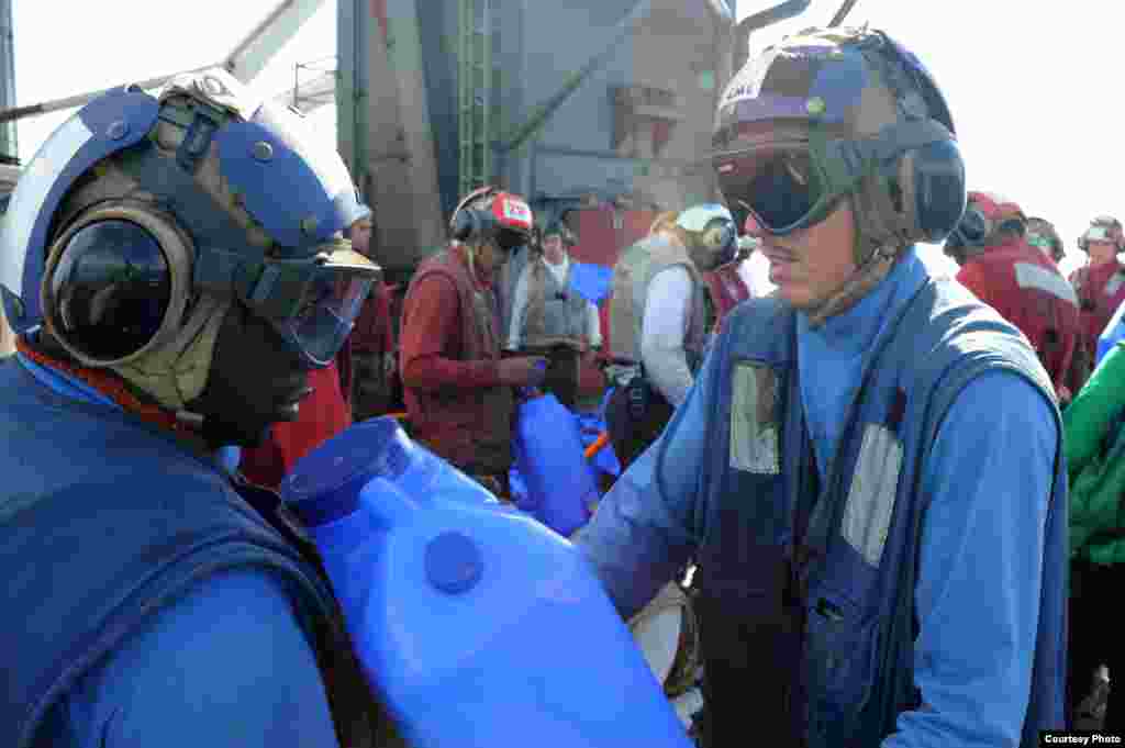 An Aviation Boatswain's Mate passes a container of fresh water for loading onto helicopters to be delivered ashore on the USS George Washington in the Philippine Sea, Nov. 16, 2013. (U.S. Navy)