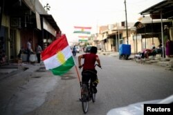 A boy rides a bicycle with the flag of Kurdistan in Tuz Khurmato, Iraq Sept. 24, 2017.