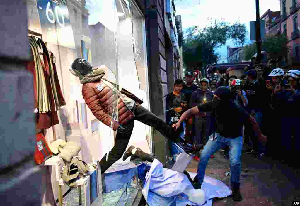 In this October 2 photo, hooded demonstrators vandalize a shop in Mexico City during the commemoration of the 50th anniversary of the 1968 Tlatelolco student massacre.