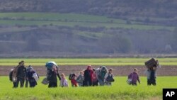 Migrants walk through a field near the northern Greek border station of Idomeni, Friday, March 4, 2016. More than 10,000 mostly Syrian and Iraqi refugees were stuck at the country's Idomeni border as Greek officials said that nearly 32,000 migrants were stranded in the country after drastically reduce of number of transiting migrants.(AP Photo/Vadim Ghirda)