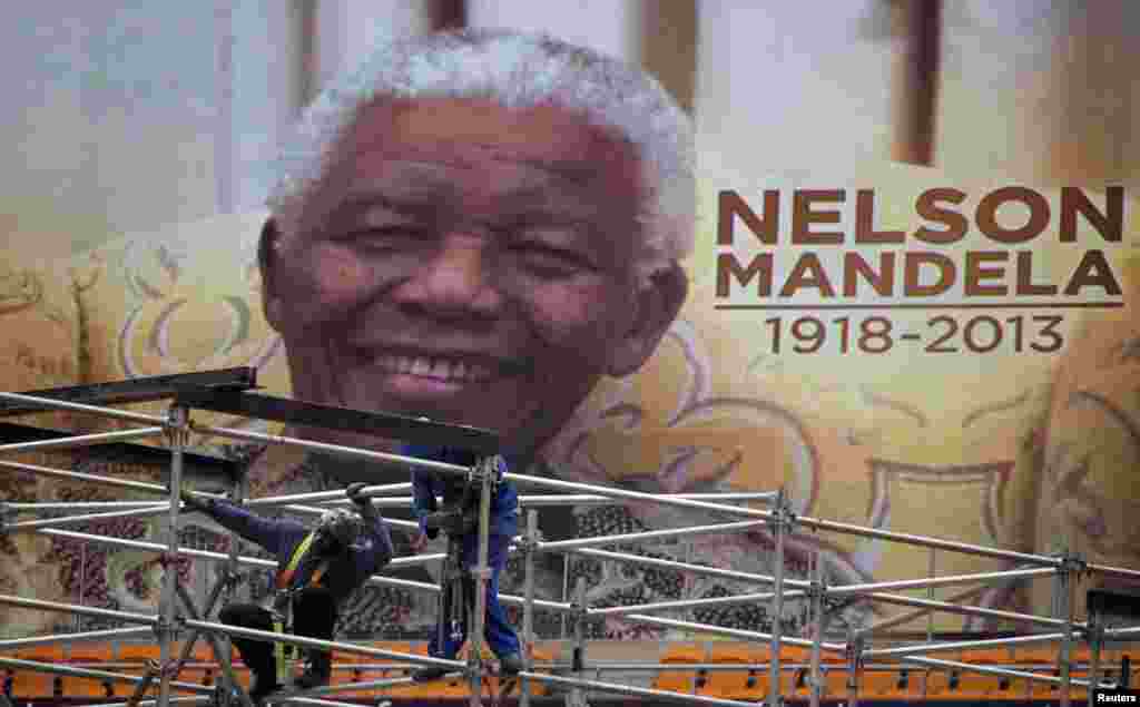 An image of Nelson Mandela is displayed on a digital screen as workers on scaffolding construct a stage ahead of Mandela's national memorial service at First National Bank (FNB) Stadium, also known as Soccer City, in Johannesburg, Dec. 9, 2013.