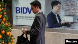 FILE - A man counts money he withdrew from an ATM machine at the headquarters of the Bank for Investment and Development of Vietnam in Hanoi.