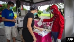 Seorang petugas pemungutan suara dengan kostum super hero membantu para pemilih di sebuah tempat pemungutan suara di Surabaya, 9 Desember 2020. (Foto: AFP)