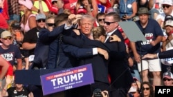 FILE - U.S. Secret Service agents surround Republican candidate Donald Trump as he is taken off the stage after an assassination attempt at a campaign event in Butler, Pennsylvania, July 13, 2024. Conspiracy theories have thrived since the event, even halfway across the world.