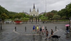 People walk past Jackson Square and St. Louis Cathedral in the French Quarter before landfall of Tropical Storm Barry from the Gulf of Mexico in New Orleans, La., July 12, 2019.