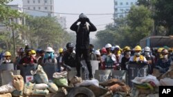 Manifestantes se escudan tras barricadas mientras la policía se reúne para enfrentarlos en Rangún, Myanmar, el domingo 7 de marzo de 2021. 